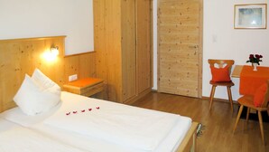 Ett sovrum med två sängar, en garderob i trä, ett skrivbord med en stol och ett litet bord med en vas.