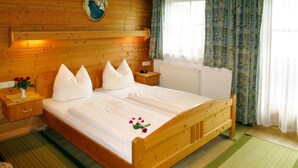A wooden bed with white linens and pillows, a nightstand with a vase of red roses, and a window with patterned curtains. - Nice apartment for 4 guests with WIFI, TV and balcony (Mitterdorf)