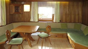 L’intérieur d’un chalet accueillant, avec une table à manger en bois, deux chaises, un banc et une fenêtre agrémentée de rideaux.