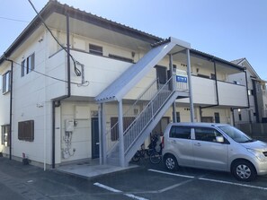 A two-story building with a staircase leading to the upper floor. There is a parked car and a bicycle near the entrance. - KASUMI-an 4 (Kumamoto)