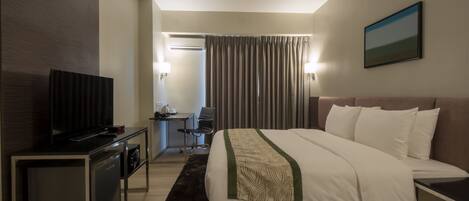 Ein Hotelzimmer mit einem Bett, einem Schreibtisch, einem Sessel, einem Fernseher und einem Bild an der Wand.