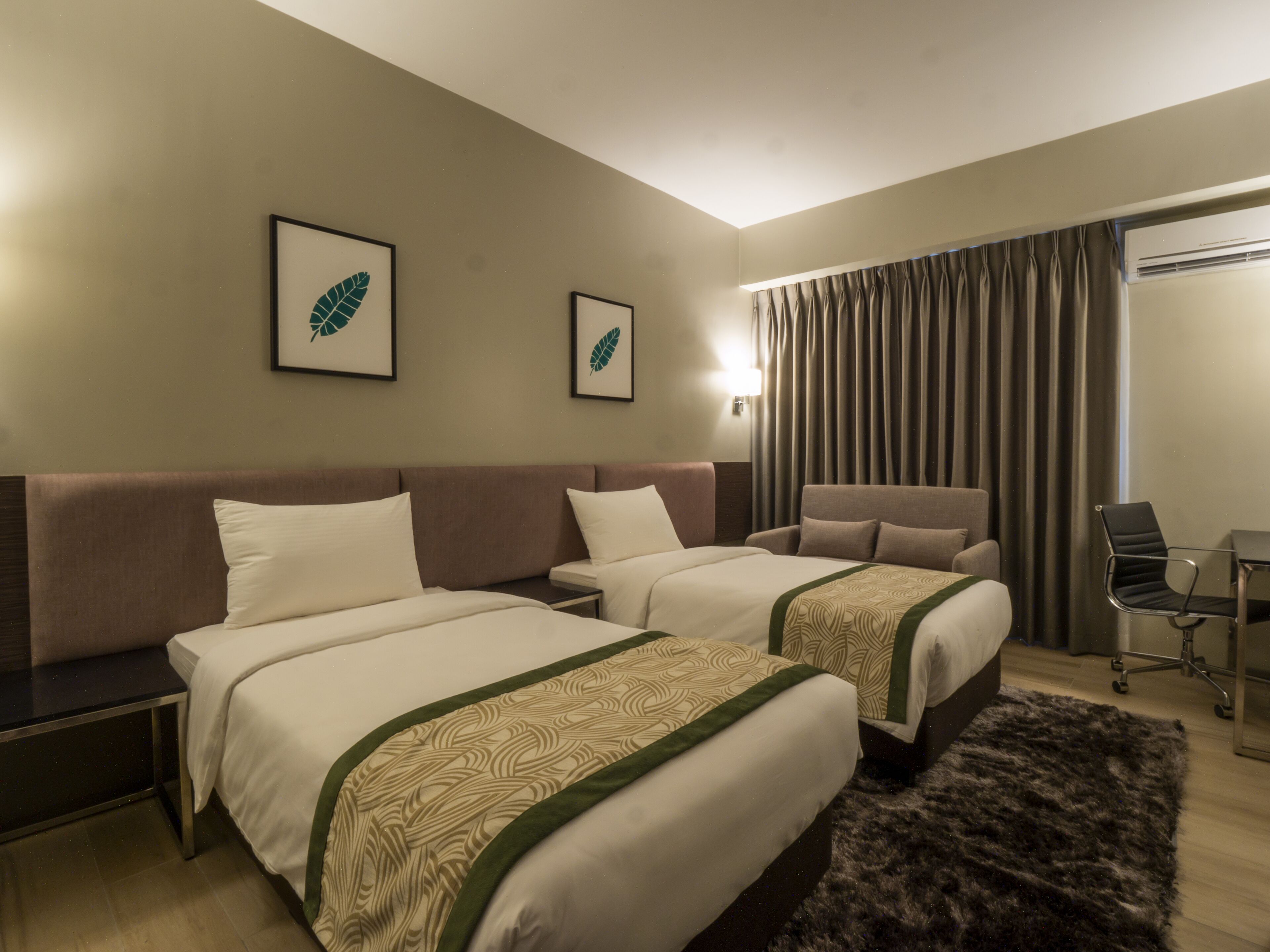 A hotel room with two beds, a desk, a chair, and a large window with curtains.