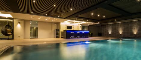 Una piscina interior con zona de bar, asientos y un diseño moderno de techo.