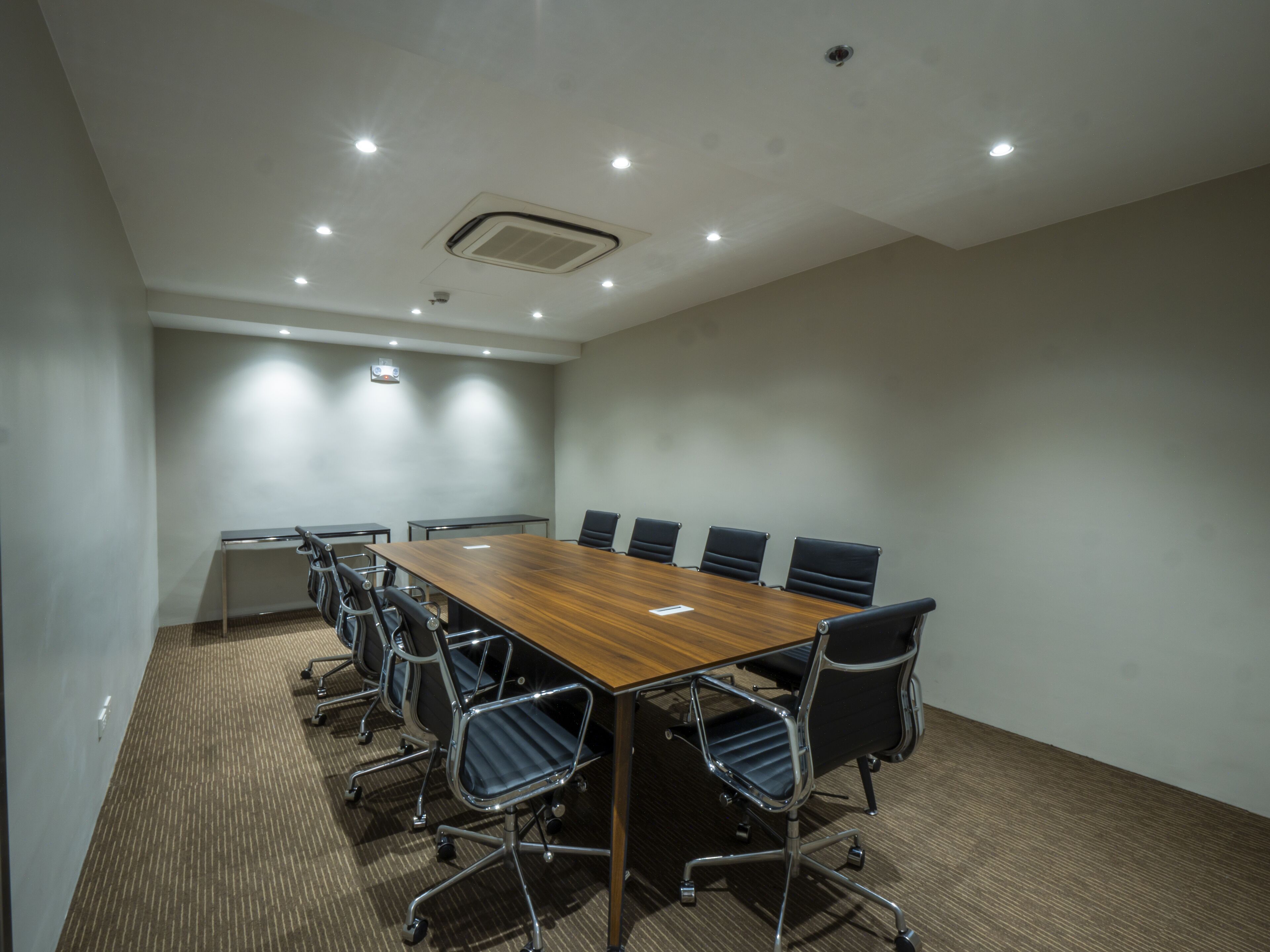 A conference room with a long table, six chairs, and a carpeted floor.