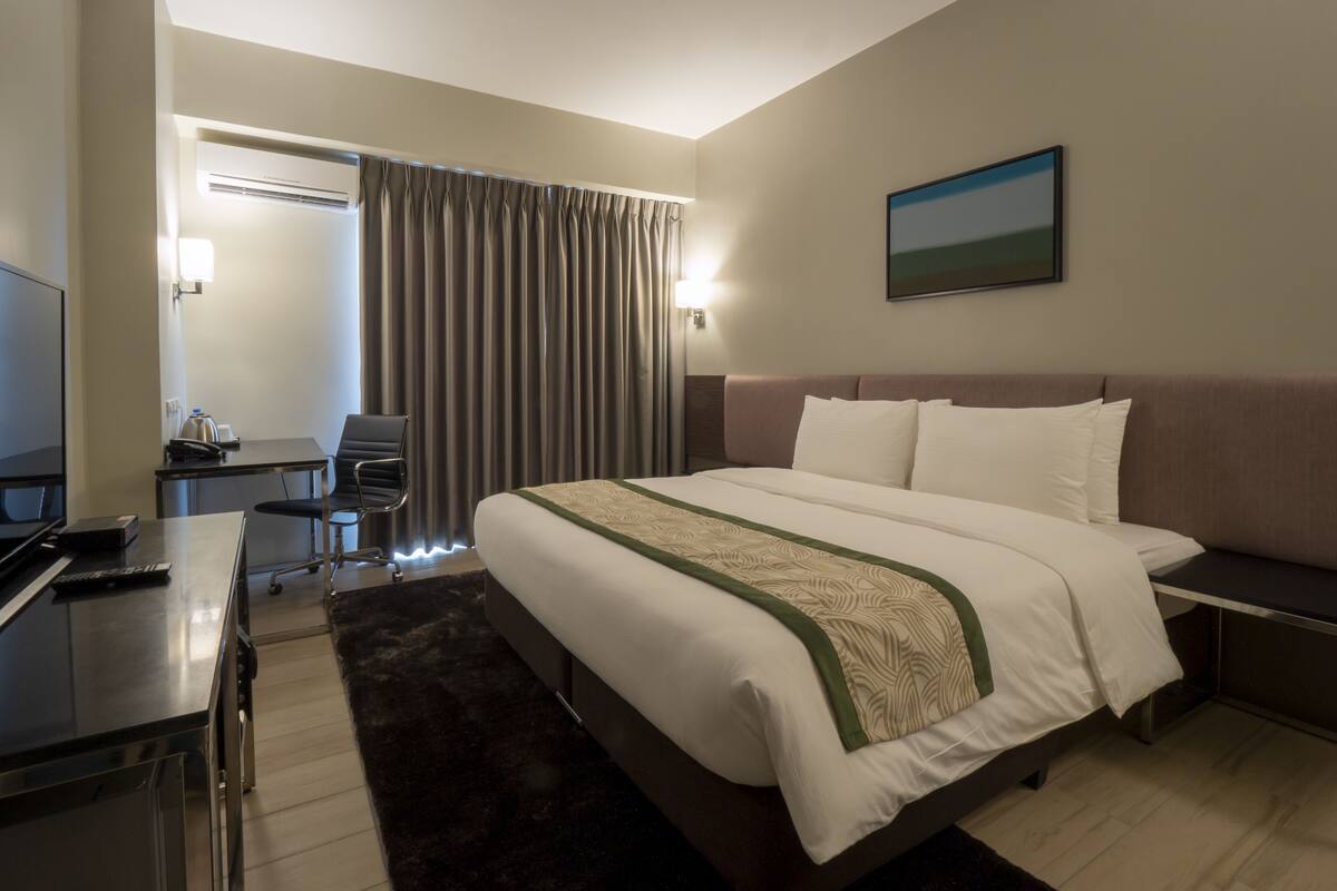 A hotel room with a bed, desk, chair, and a painting on the wall.