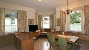 Ein gemütliches Wohnzimmer mit einer hölzernen Bank, einem Esstisch mit Stühlen, einem Fernseher und einer Pendelleuchte.