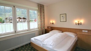 Ein Hotelzimmer mit Doppelbett, zwei Nachttischen, einer Heizung, einem Fenster mit Vorhängen und zwei Wandlampen.