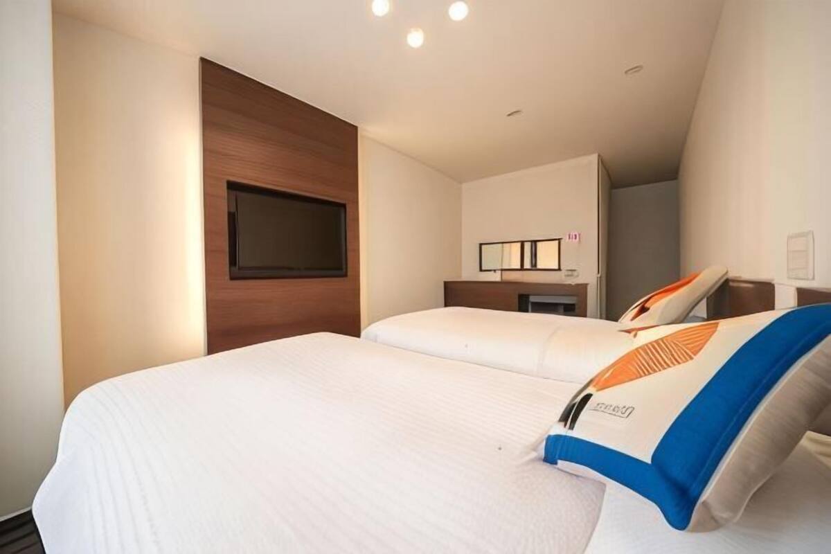 A hotel room with two beds, a flat-screen TV, a bedside table, and a mirror.