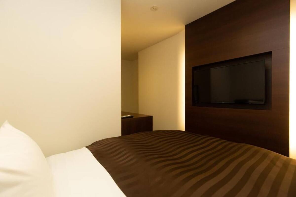 A hotel room with a bed, a television mounted on the wall, and a bedside table.