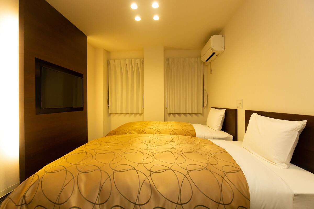 A hotel room with a bed, a TV mounted on the wall, and an air conditioning unit.