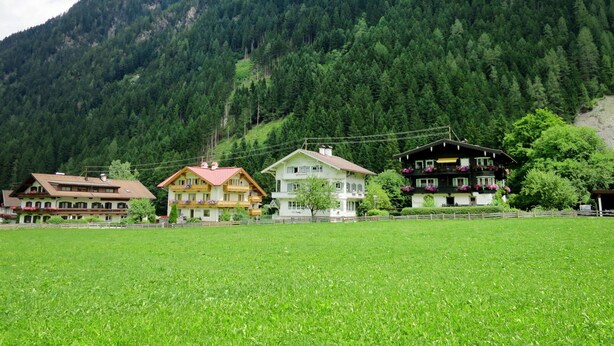 A row of traditional wooden houses with balconies, set against a backdrop of a dense forest and a mountain. - Cosy apartment for 6 people with WIFI, TV and balcony (Mayrhofen)