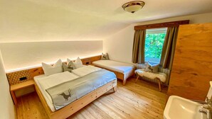 Un dormitorio con dos camas, piso de madera, una ventana con cortinas y un lavamanos.