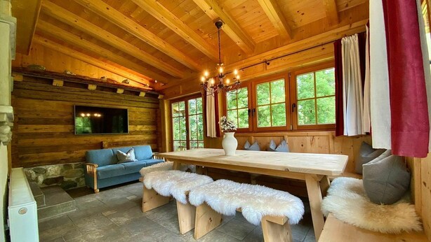 Interior acogedor de una cabaña con una mesa de comedor de madera, bancos, un sofá y un televisor montado en la pared.
