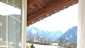 Una silla amarilla con estructura metálica en una habitación con suelo de madera, una ventana con vistas a montañas y un techo de madera.