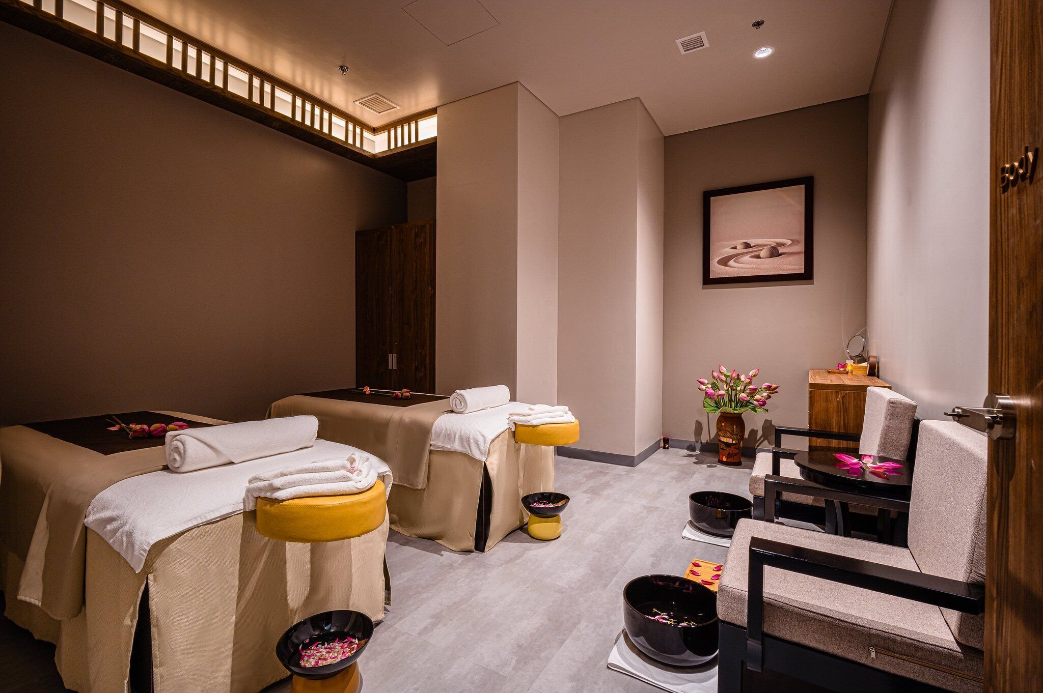 A spa room with two massage tables, a wooden cabinet, and a small seating area.
