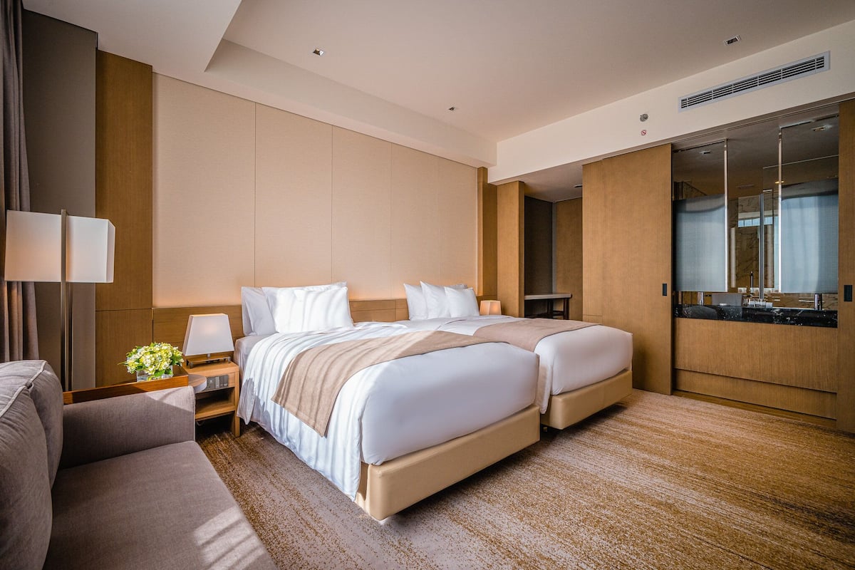 Ein modernes Hotelzimmer mit einem großen Bett, einer Couch, einem Schreibtisch mit Lampe und einem Spiegel.