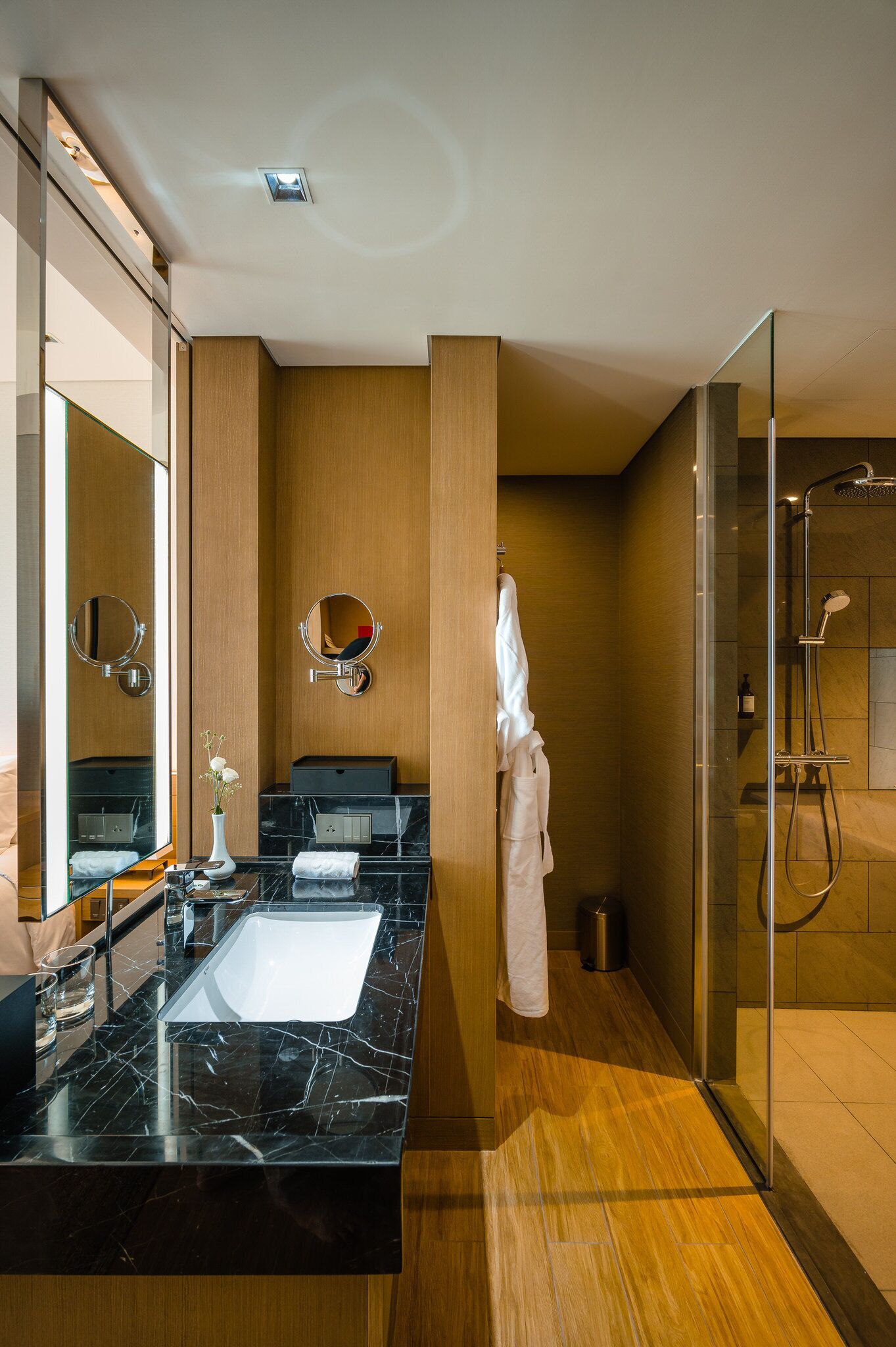A modern bathroom with a black marble sink, two mirrors, a glass shower enclosure, and a wooden vanity.