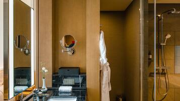 A modern bathroom with a black marble sink, two mirrors, a glass shower enclosure, and a wooden vanity.