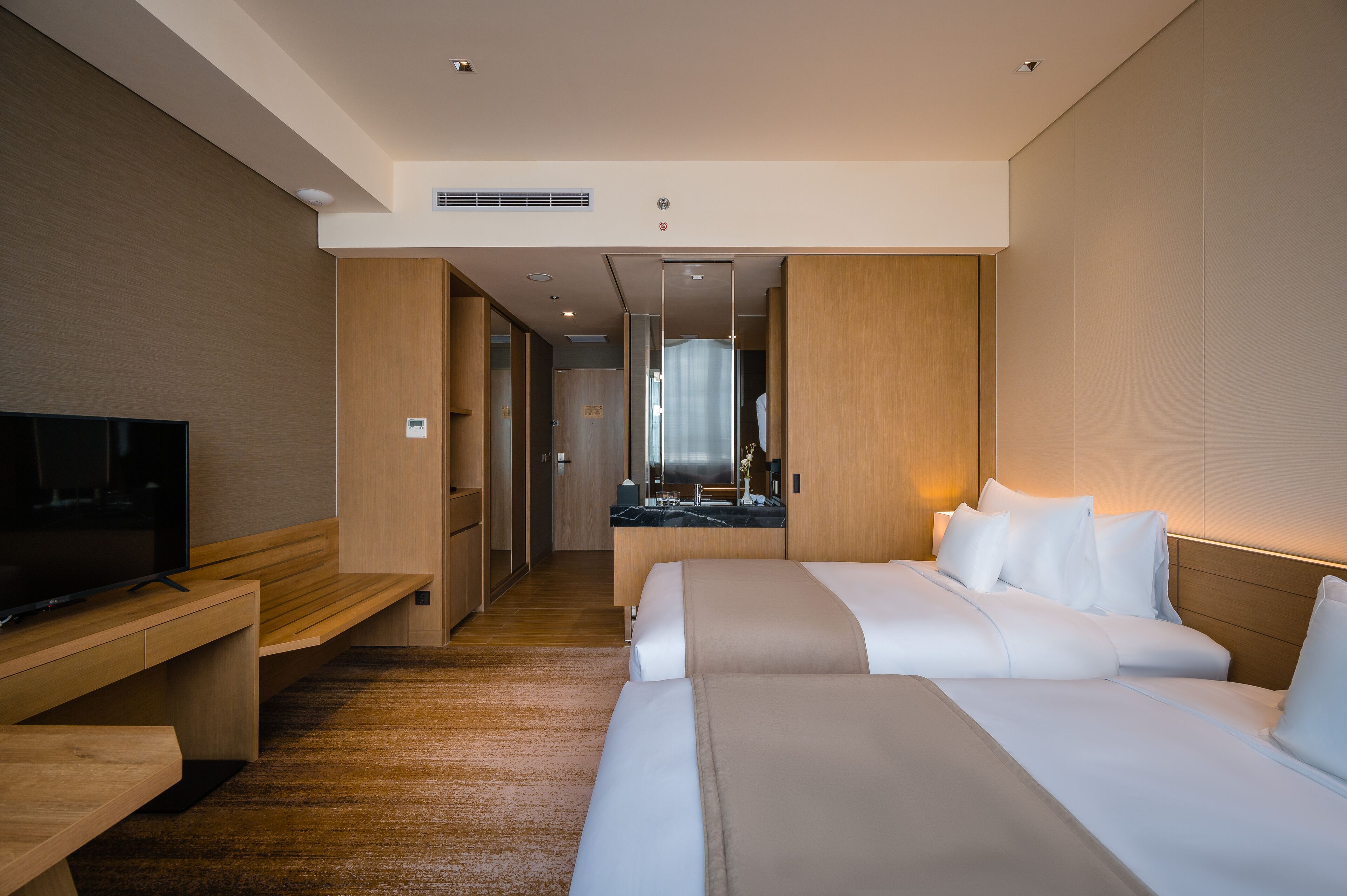 A modern hotel room with a large bed, a TV on a wooden bench, and a bathroom visible through an open door.