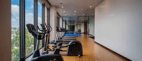 Un gimnasio con máquinas de cardio, ventanas amplias y vistas a la ciudad.
