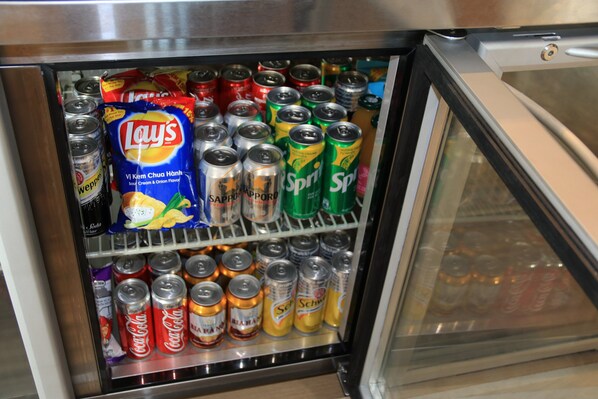 Un refrigerador lleno de bebidas, incluyendo latas de refresco y papas fritas.