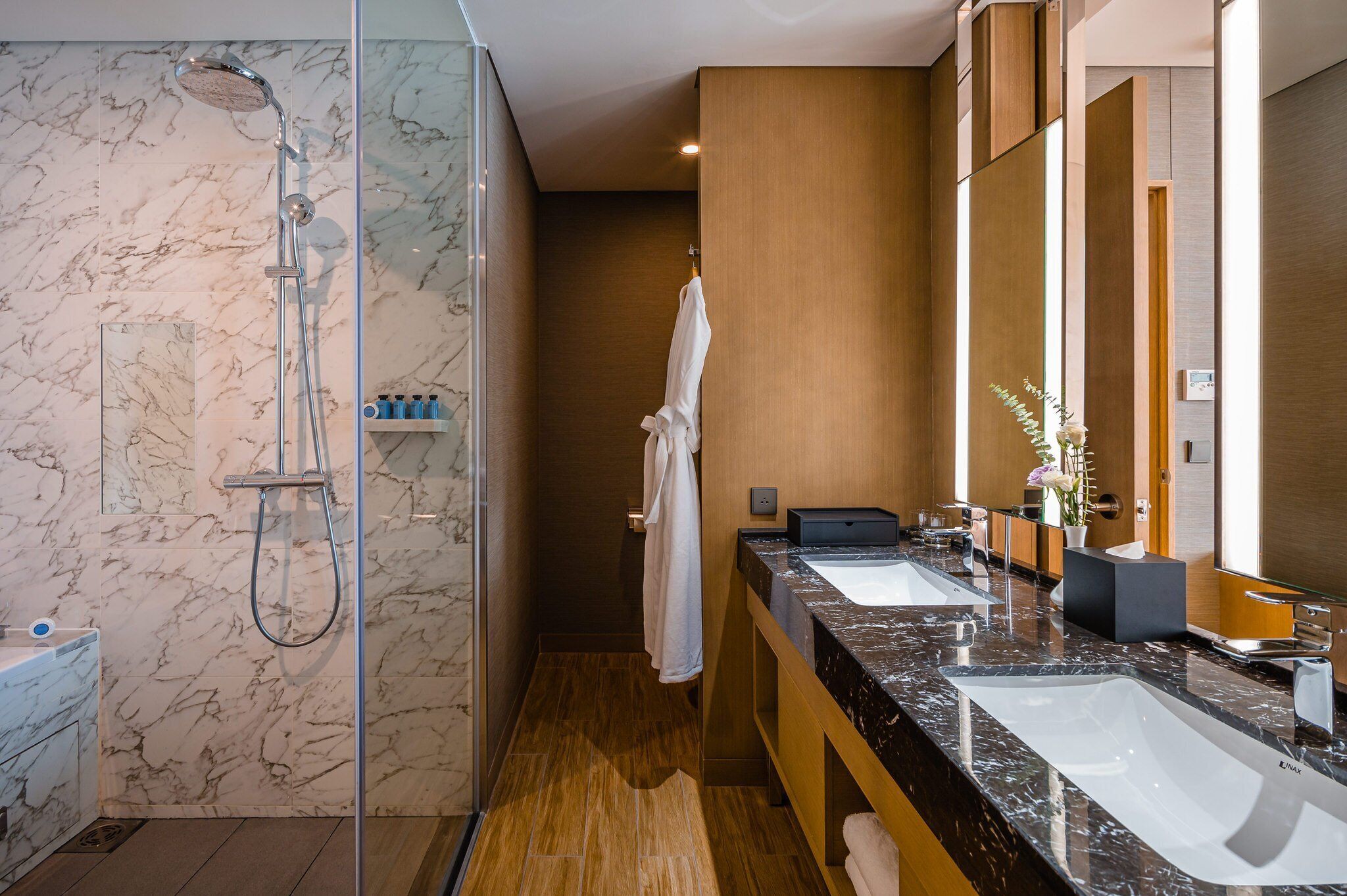 Une salle de bain moderne dotée d’une douche à parois de verre, de deux vasques et d’un meuble-lavabo en bois.
