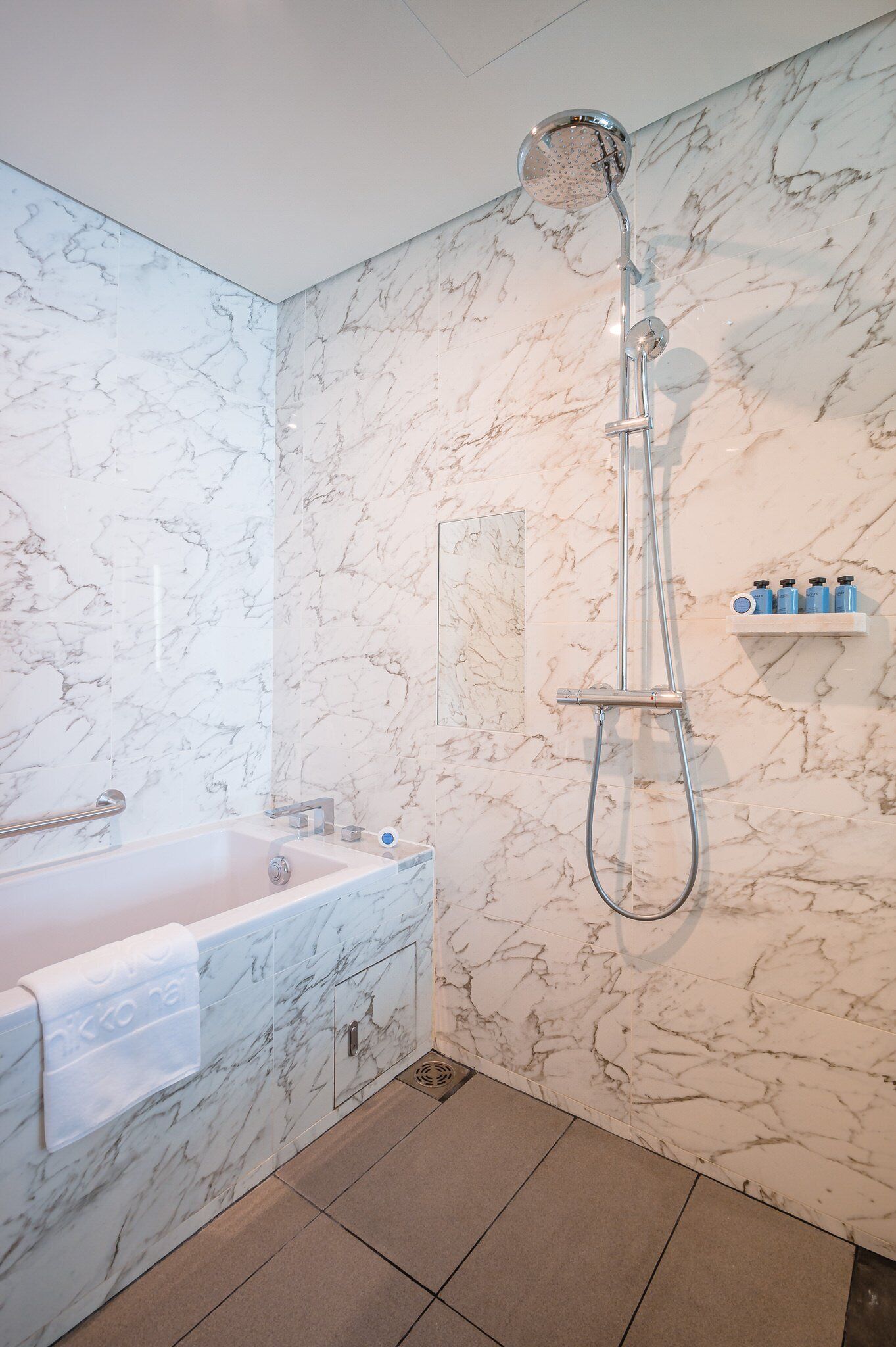 Une salle de bain avec un mur en marbre, une baignoire, une douche et une étagère contenant des articles de toilette.