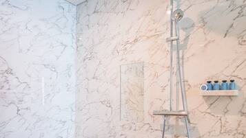Une salle de bain avec un mur en marbre, une baignoire, une douche et une étagère contenant des articles de toilette.