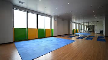 A spacious room with large windows, a blue mat area, and exercise equipment.