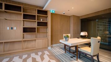 A modern office space with a wooden shelving unit, a white table with a lamp, and a patterned carpet.