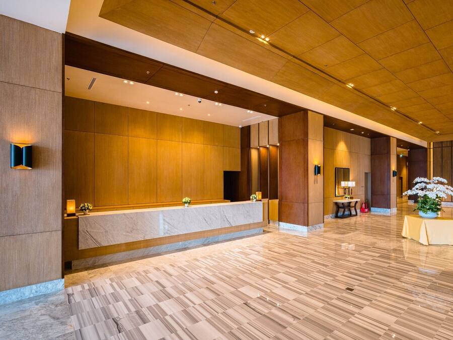 Un moderno vestíbulo de hotel con una recepción de mármol, paneles de madera y un suelo de mármol pulido.