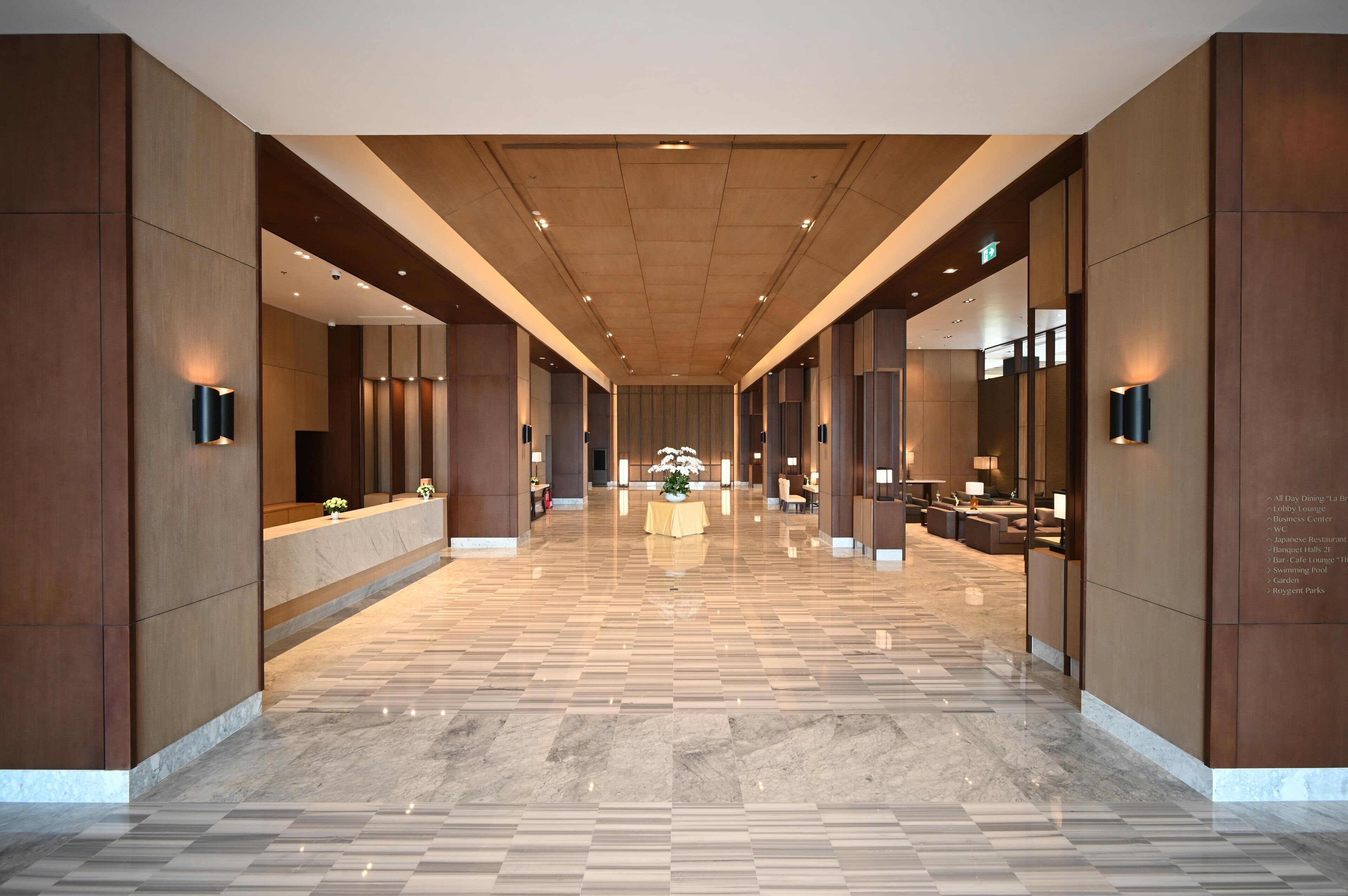A spacious, modern hotel lobby with a polished marble floor, wooden paneling, and contemporary lighting fixtures.