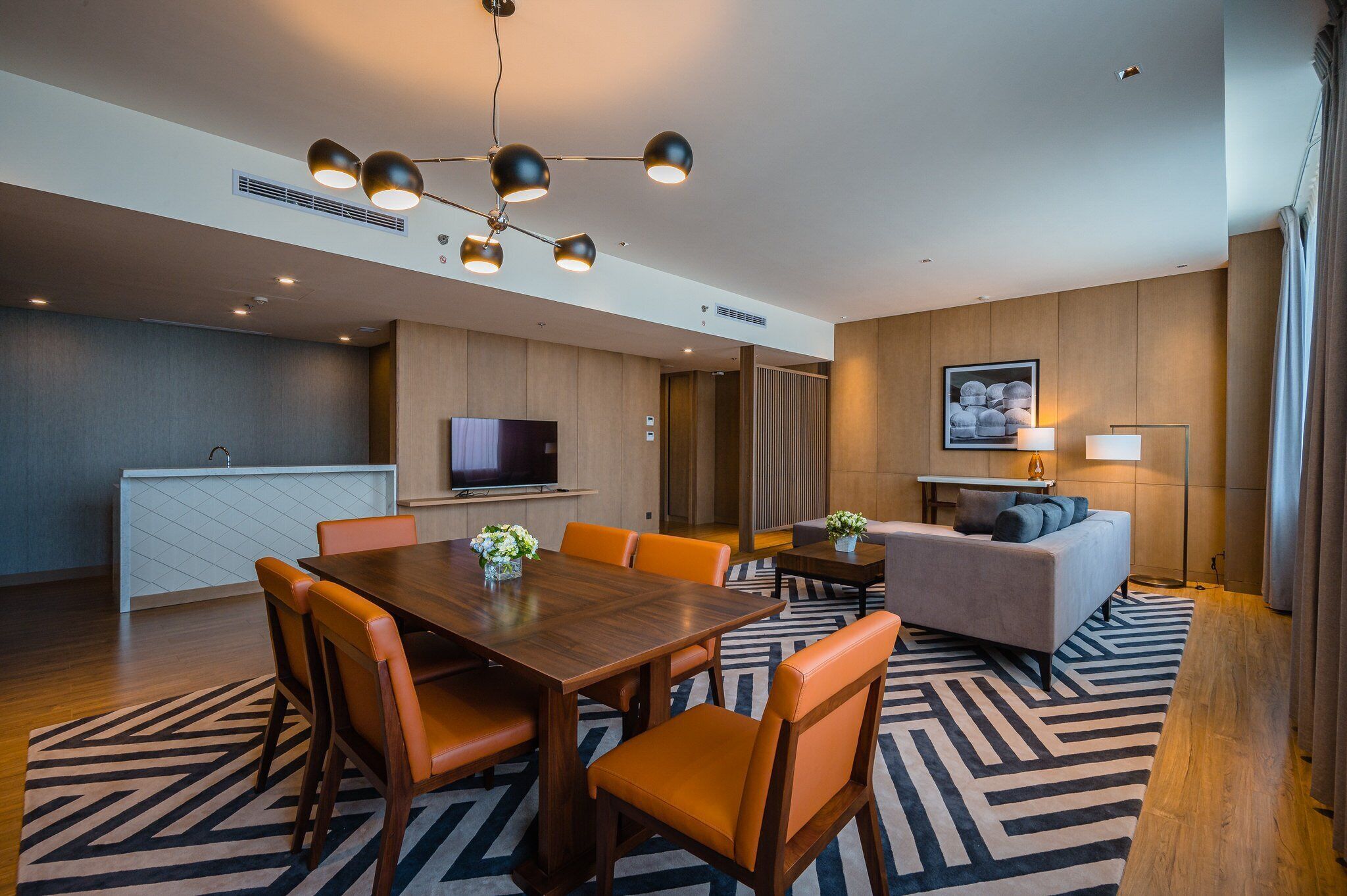 A modern hotel room with a dining area, a sofa, a TV, and a lamp.