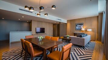A modern hotel room with a dining area, a sofa, a TV, and a lamp.