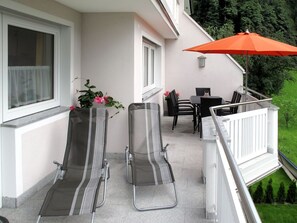 Relax on the balcony with two comfortable chairs and a small table, overlooking a serene grassy area with trees.