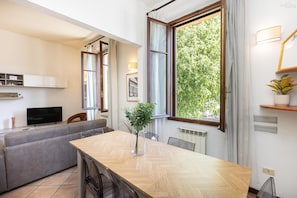 A modern living room with a sofa, a dining table, a TV, and a large window with curtains.