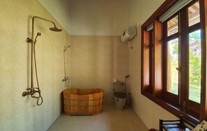 Une salle de bain avec une baignoire en bois, une douche et des toilettes. Une fenêtre laisse entrer la lumière naturelle.