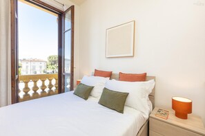 Une chambre d’hôtel avec un lit, une table de chevet, un tableau encadré au mur et un balcon avec une balustrade.