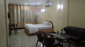 A hotel room with a bed, a table with chairs, a sofa, an air conditioning unit, and a curtain with a floral pattern. - Nemarts Hotel (Dar es Salaam)