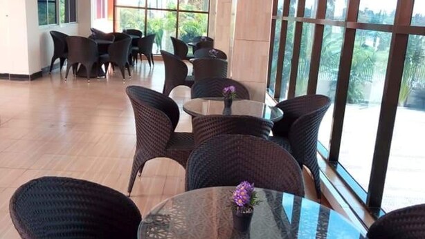 A spacious indoor area with high ceilings and large windows, featuring wicker furniture and a glass table with a purple flower centerpiece. - Nemarts Hotel (Dar es Salaam)