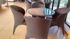 A seating area with wicker chairs and a glass table, large windows, and a tiled floor. - Nemarts Hotel (Dar es Salaam)