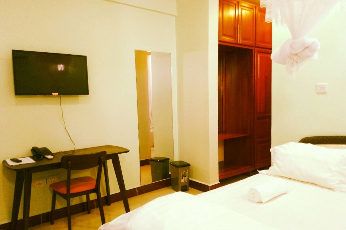 Habitación de hotel con cama, escritorio con silla, televisor, armario y cubo de basura.