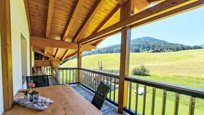 A wooden deck with a table and chairs, overlooking a green field and hills. - Nice apartment for 4 people with WIFI, TV and balcony (Wildschönau)