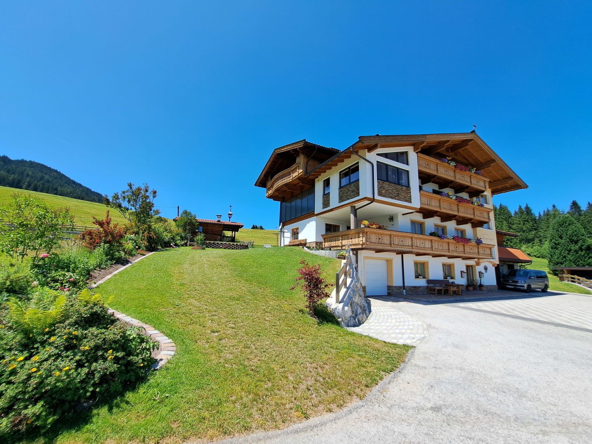 Un chalet à plusieurs étages doté de balcons en bois, d’une allée pavée et surplombant un paysage montagneux.