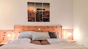 Un lit avec une tête de lit en bois, plusieurs oreillers et une couverture moelleuse. Il y a deux lampes de chevet et un tableau accroché au mur au-dessus du lit.