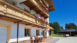 Un chalet traditionnel avec des fondations en pierre, des balcons en bois ornés de jardinières et une terrasse dallée avec des meubles d’extérieur.