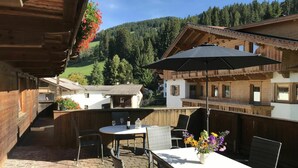 A wooden chalet with a patio area featuring a table, chairs, and a black umbrella. - Cosy apartment for 4 guests with WIFI, TV, terrace and panoramic view (Wildschönau)