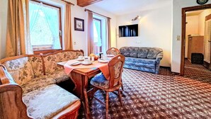 A dining area with a wooden table and chairs, a sofa, and a television on the wall. - Cosy apartment for 4 guests with WIFI, TV, terrace and panoramic view (Wildschönau)