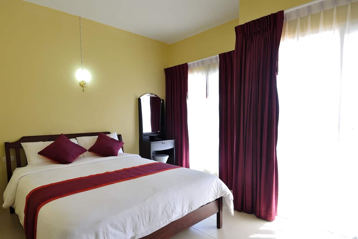 Una habitación de hotel con una cama grande, una mesita de noche, un espejo y una ventana con cortinas.