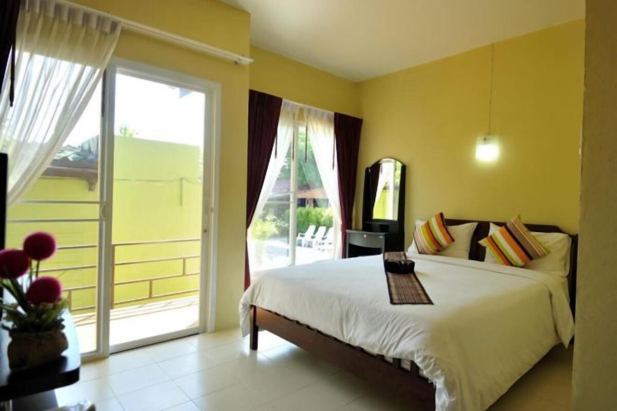 A hotel room with a bed, a nightstand, a mirror, and a view of the outside.